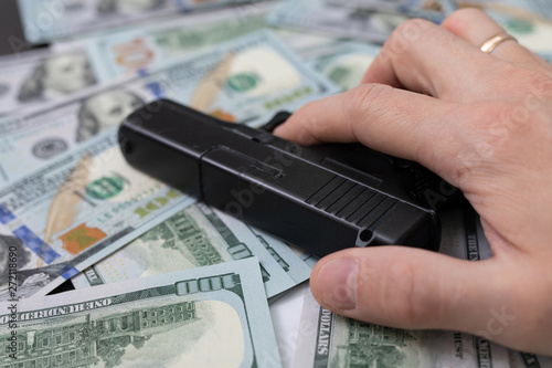 hand holding a gun lies on a pile of money