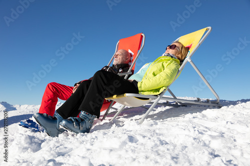 Senior couple  sunbathing in a deckchair near a snowy ski slope