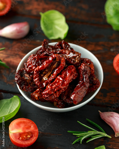 Sun dried tomatoes in white bowl with fresh herbs and spices on wooden table