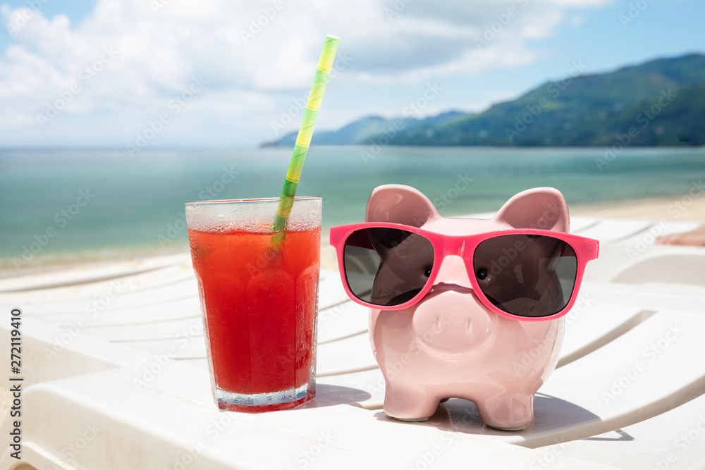 Juice Glass And Piggybank On Deck Chair At Beach
