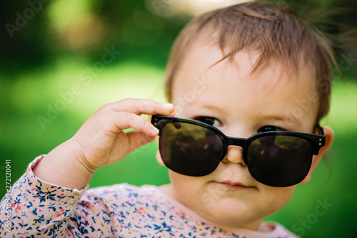 Baby with sunglasses on the green grass background on a sunny day, lifestyle