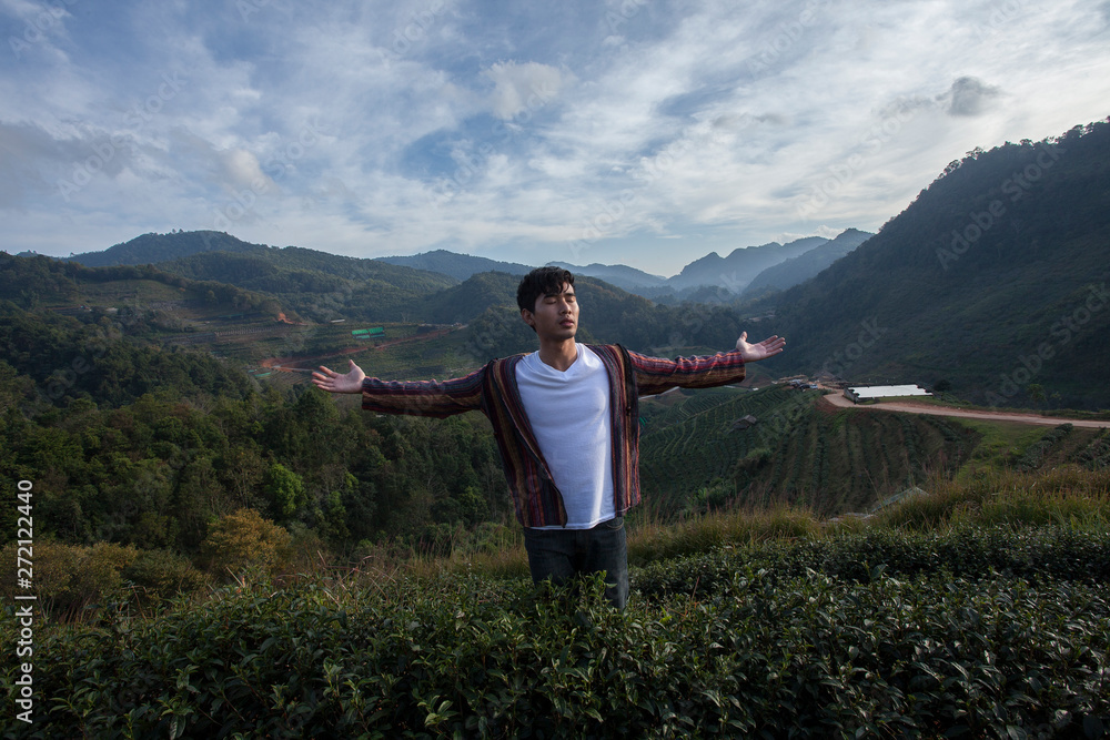Standing with his back a man traveler extend the arm so happy with sunrise and the fresh air in green tea field on the mountains.