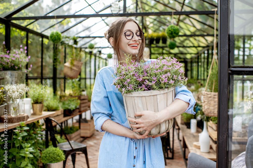 Obraz premium Portrait of a young woman standing with lavender at the entrance of the beautiful greenhouse or flower shop