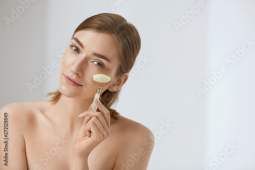 Beauty skin care. Woman using jade roller for face massage