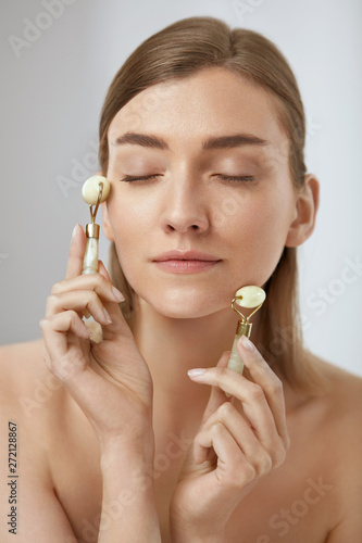 Beauty face care. Woman doing facial massage with jade rollers
