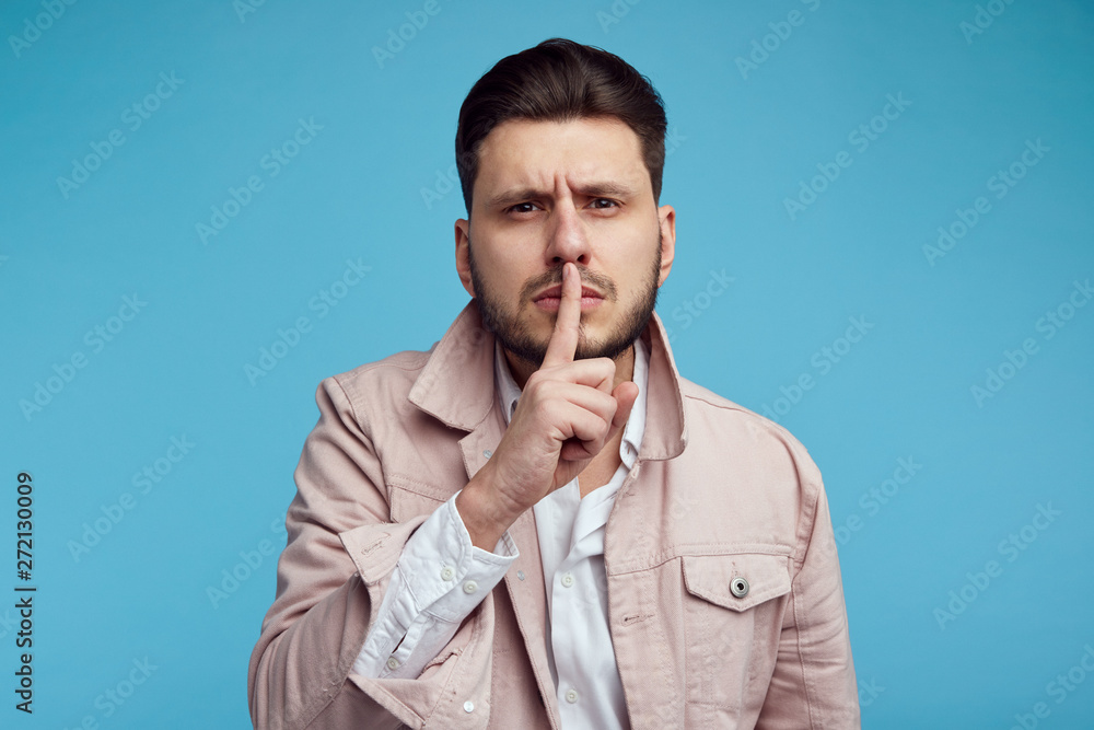 Attractive man shows hush gesture, looks with stunned expression at camera, afraids of gossiping, isolated over blue background. Attractive man shows hush gesture, looks with stunned expression at camera, afraids of gossiping, isolated over blue background.
