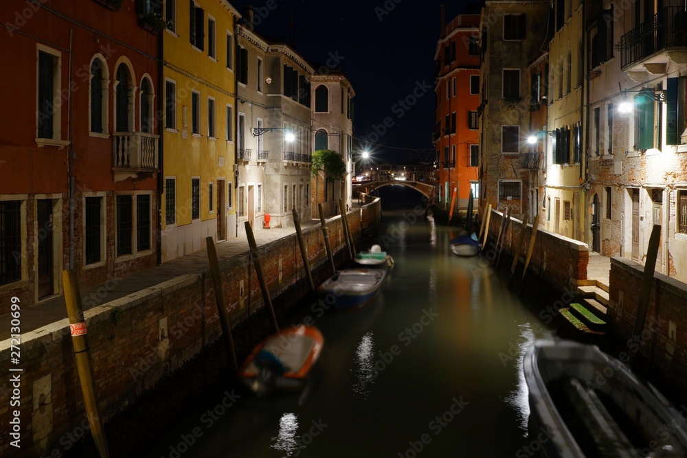 Night view of a quiet venetian canal with moored boats and street lights