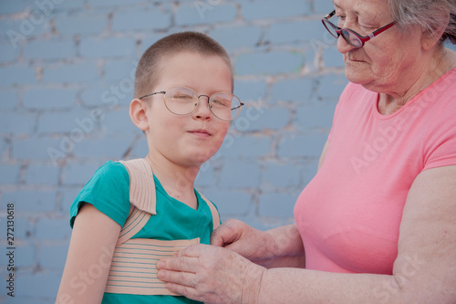 elderly woman in pink T-shirt and glasses wears corset to correct posture for her grandson. child is happy that grandmother loves him and cares