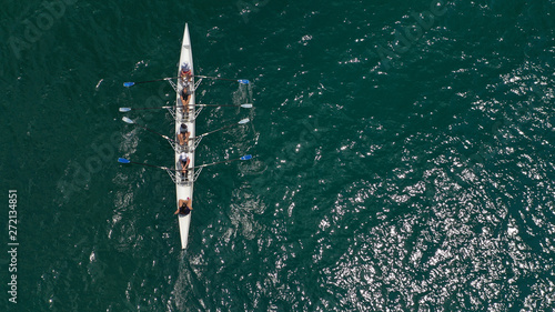 Aerial drone bird's eye view of sport canoe operated by team of young trained athletes in deep blue Aegean sea