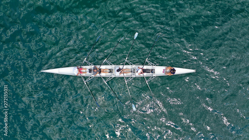 Aerial drone bird's eye view of sport canoe operated by team of young trained athletes in deep blue Aegean sea