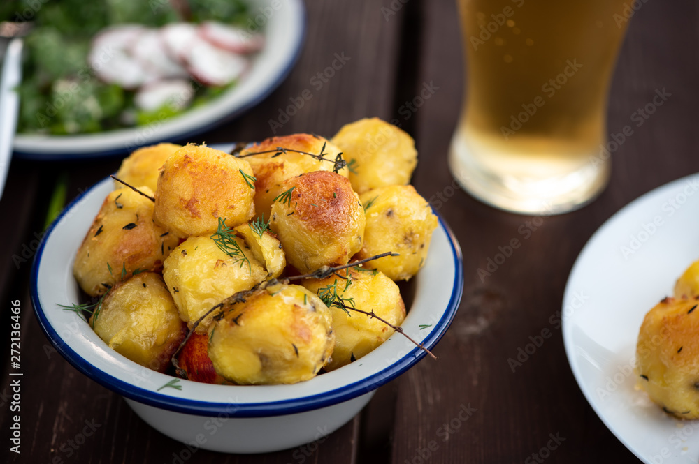 Baked potatoes with herbs on a wooden table in the garden. Delicious vegetarian food outdoors, country lunch. Baked potatoes with herbs on a wooden table in the garden. Delicious vegetarian food outdoors, country lunch.