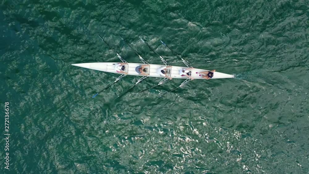 Aerial drone bird's eye view video of sport canoe operated by team of young women in emerald open ocean sea Aerial drone bird's eye view video of sport canoe operated by team of young women in emerald open ocean sea