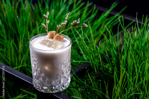 Beautiful white cocktail based on Jack Daniels Honey, milk and macadamian syrup with ice in a faceted glass on the background of fresh greens. Close-up photo