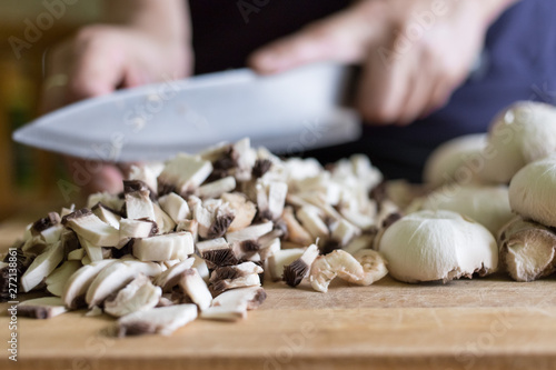 A woman cuts mushrooms with a knife on a wooden cutting board