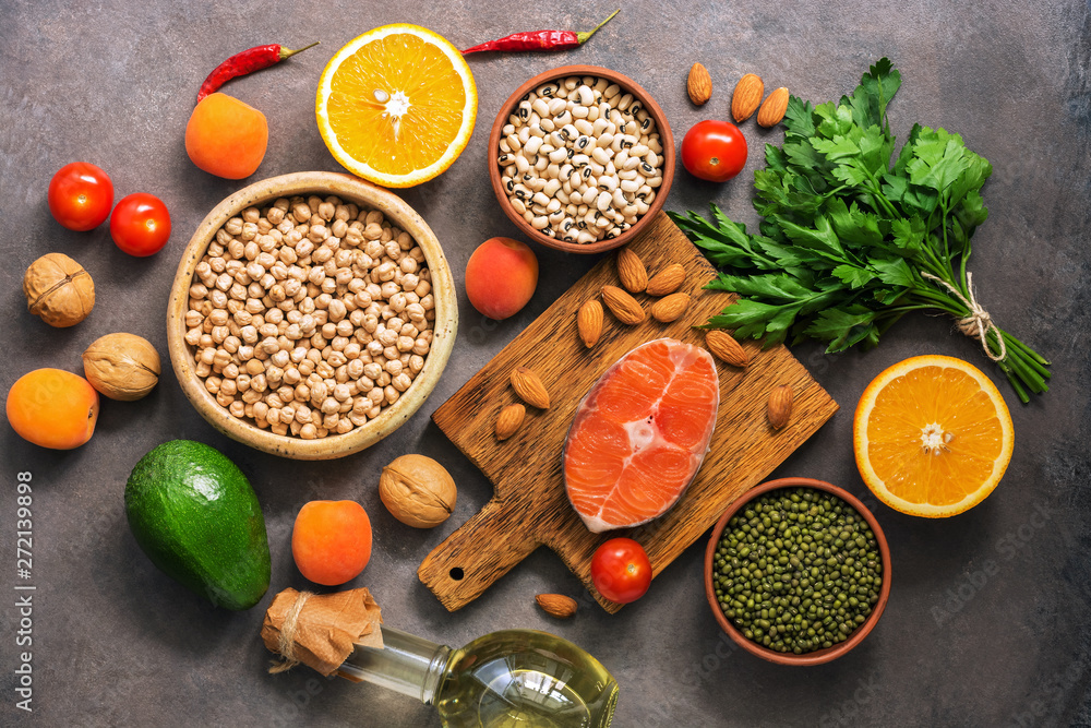 Concept healthy balanced food, salmon,legumes, fruits, vegetables, olive oil and nuts, dark rustic background. Flat lay, top view.