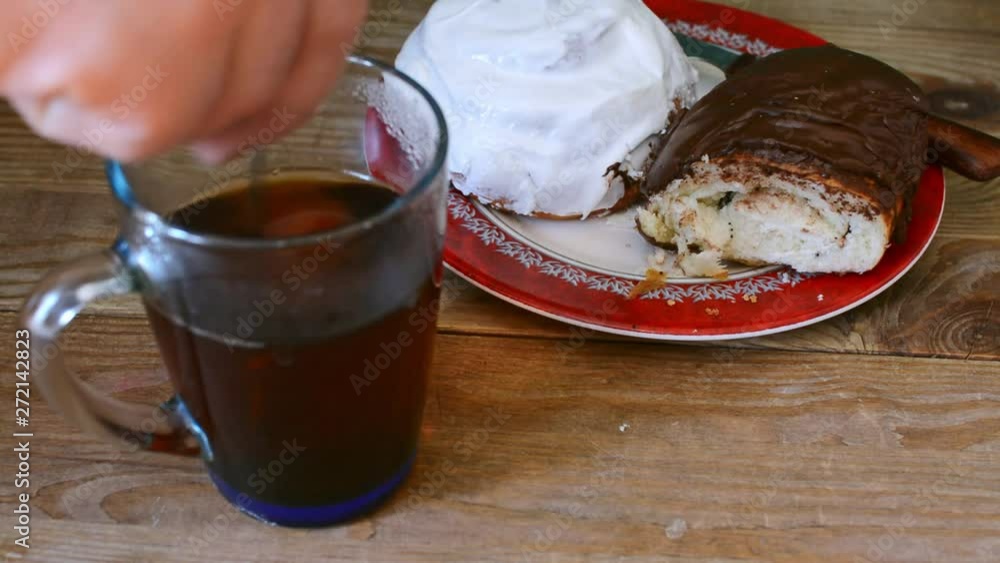 A man is stirring sugar in a cup with tea. Sweet donut and bagel on a plate on wooden table. A man is stirring sugar in a cup with tea. Sweet donut and bagel on a plate on wooden table.
