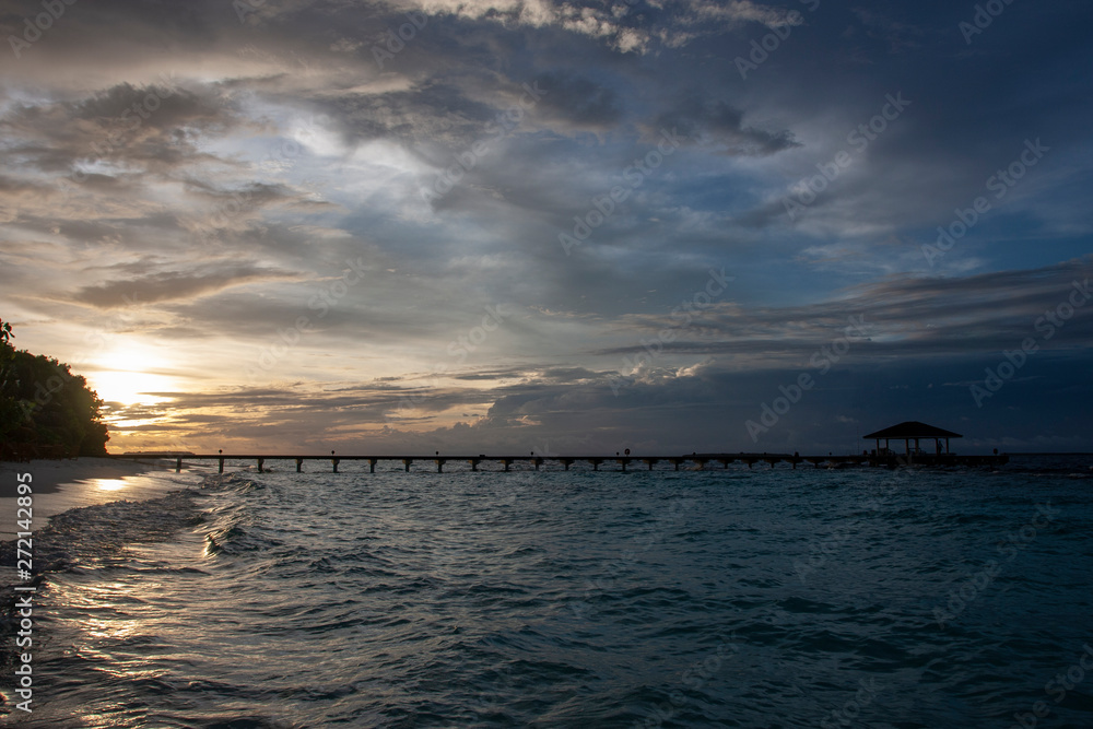 Silhouette of the long pier, bridge,  on the background of a sunset on Maldives Islands. Night landscape. 