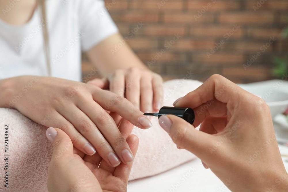 Fototapeta premium Manicurist applying polish on client's nails at table, closeup. Spa treatment
