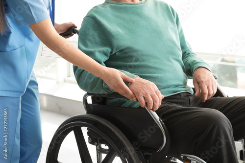Nurse assisting senior man in wheelchair at hospital, closeup