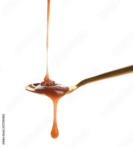 Tasty caramel sauce pouring into spoon isolated on white