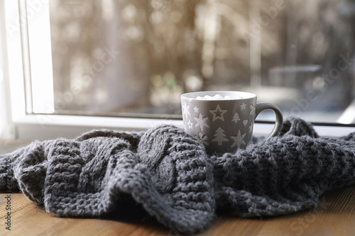 Cup of winter drink and knitted scarf on windowsill. Space for text