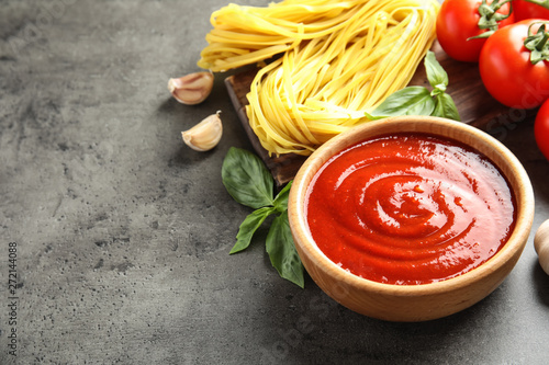 Bowl of tasty tomato sauce and pasta served on grey table. Space for text