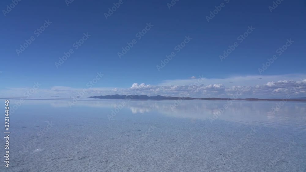 Salar de Uyuni Zoom Out establishing shot of salt flats covered in rain water, clear blue sky reflecting in clear blue water and mountains on horizon. looks like heaven in Bolivia, Latin America