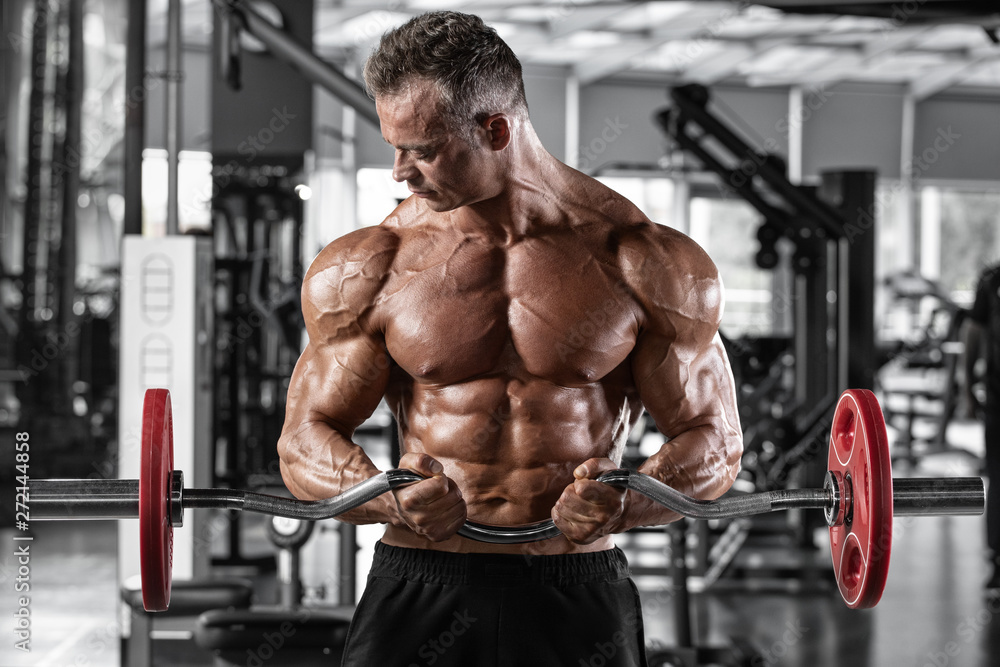 Muscular man workout in gym doing exercises with barbell for biceps, strong male naked torso abs Muscular man workout in gym doing exercises with barbell for biceps, strong male naked torso abs