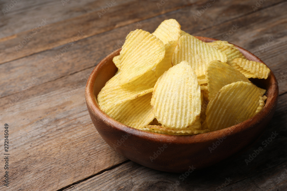 Delicious crispy potato chips in bowl on table, space for text Delicious crispy potato chips in bowl on table, space for text