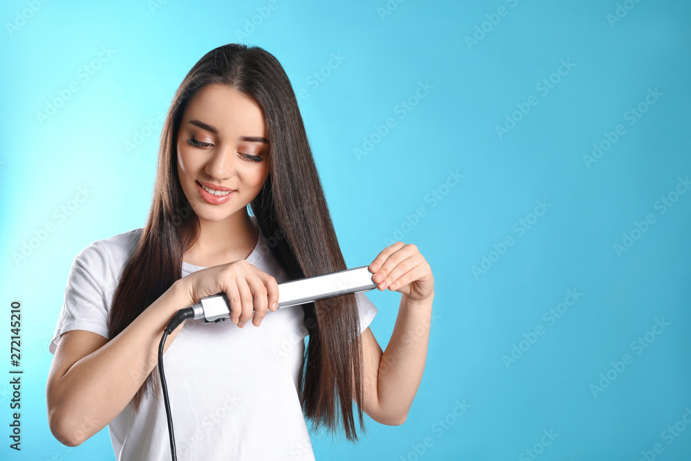 Happy woman using hair iron on color background. Space for text Happy woman using hair iron on color background. Space for text