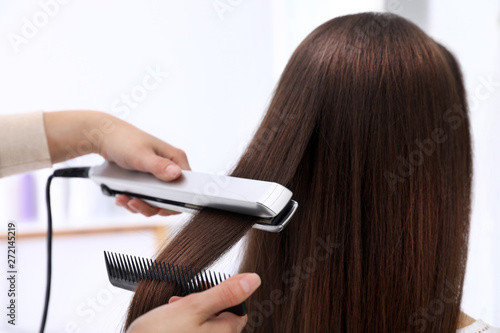 Hairdresser using modern flat iron to style client's hair in salon