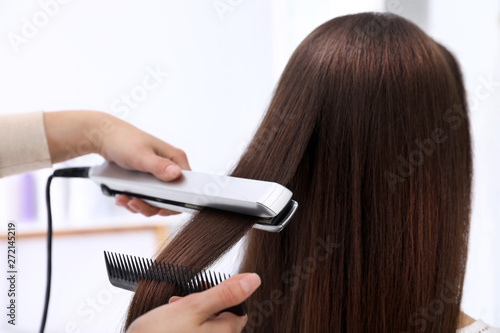 Hairdresser using modern flat iron to style client's hair in salon photo