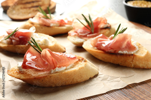 Tasty bruschettas with prosciutto and cream cheese on parchment, closeup