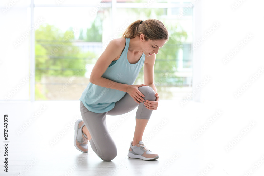 Fototapeta premium Woman in sportswear suffering from knee pain at gym