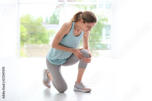 Woman in sportswear suffering from knee pain at gym