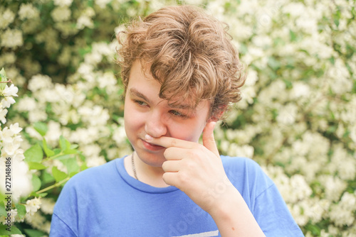 Teenager with allergies standing in a blue t-shirt among the Jasmine bushes and suffers from bad health