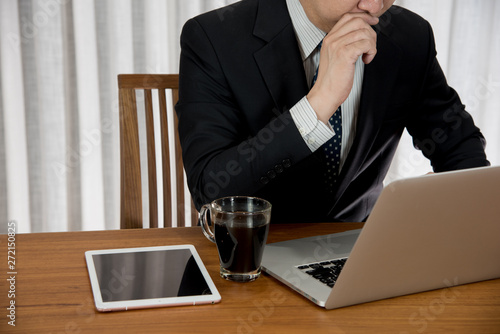 Businessman working at laptop with a cup of coffee. Businessman thinking and sitting on teak wood table.