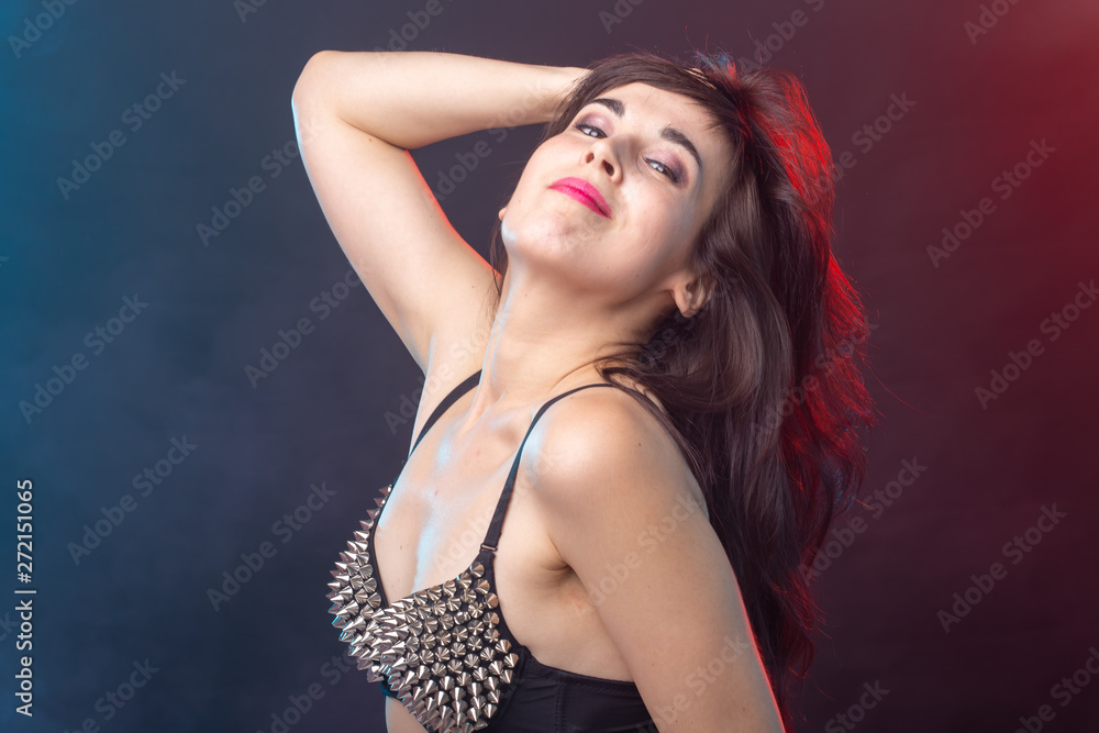 Attractive young sexy brunette woman in riveted top posing in the studio on a dark background.