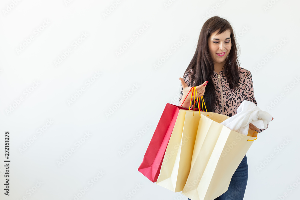 Charming young joyful brunette woman holds in her hands bags with a new clothing posing on a white background with copy space