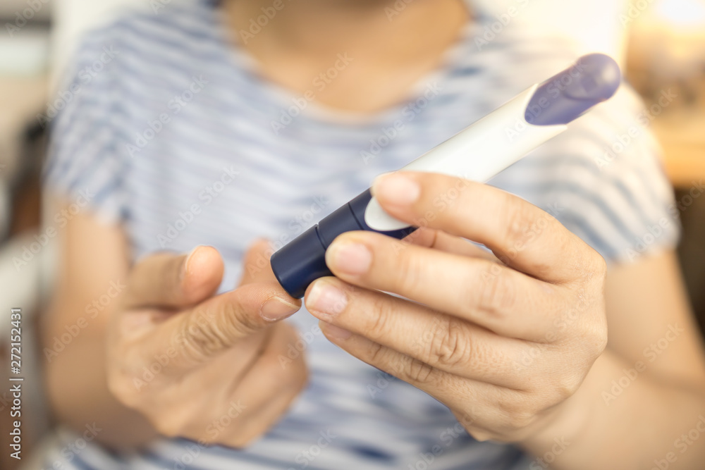 Fototapeta premium Close up of woman hands using lancet on finger to check blood sugar level by Glucose meter. Use as Medicine, diabetes, glycemia, health care and people concept.