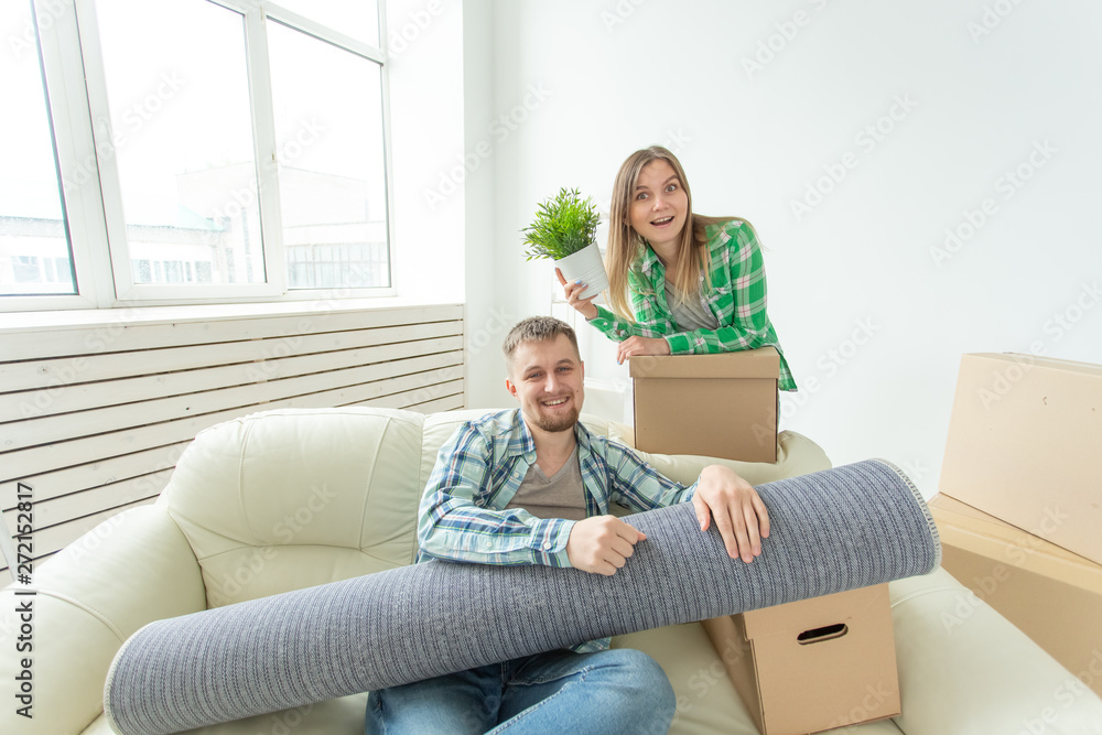 Satisfied cheerful young couple strong man and pretty woman holding their things in their hands sitting in the living room of a new apartment. Housewarming concept.