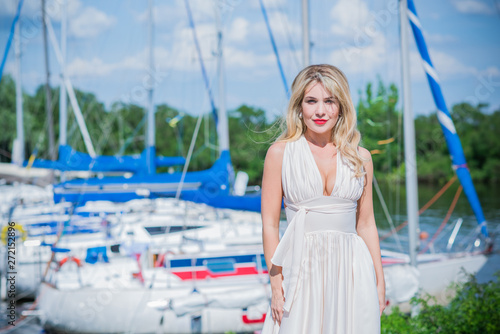 Nice blonde lady in yacht club. Woman in flying silk white dress at outdoor, relax time