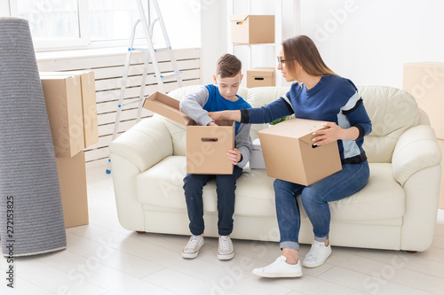 Cute mom and little boy son sort boxes with things after the move. The concept of housewarming mortgage and the joy of new housing.