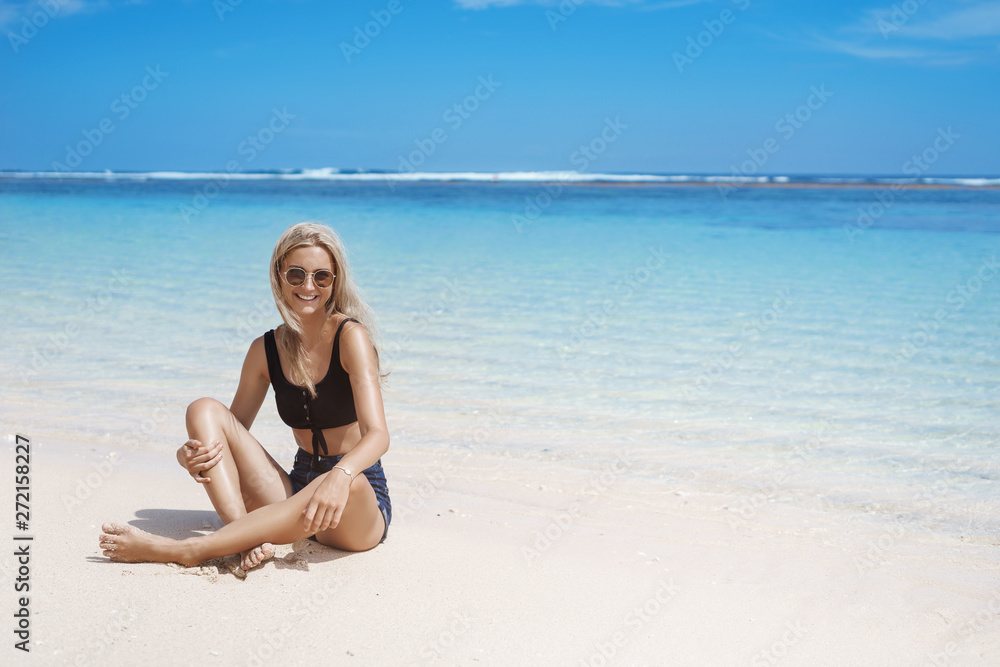 Happy smiling blond woman shorts, cropped-top sunglasses sunbathing joyfully enjoy travelling ocean sit sandy beach near shore blue waves, sky, look camera amused, relaxing tourist have fun Happy smiling blond woman shorts, cropped-top sunglasses sunbathing joyfully enjoy travelling ocean sit sandy beach near shore blue waves, sky, look camera amused, relaxing tourist have fun