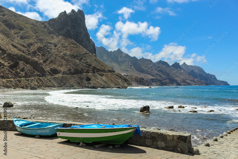 Panoramic view of Aimasiga beach with volcanic black sand and lone rocks sticking out of the sea foam. Local fishing boats in the foreground. North coast of the island Tenerife, Spain