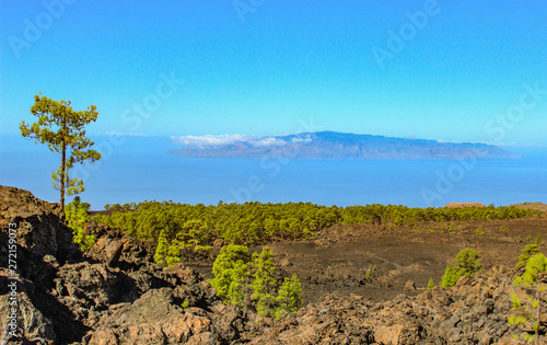 Island of La Gomera, soaring over the horizon, partly covered by the clouds. Bright blue sky. View from 1900 meters of altitude. Teide National Park, Tenerife, Canary Islands, Spain.