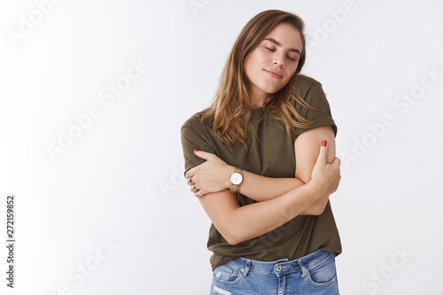 Tenderness, love, acceptance concept. Cute feminine carefree attractive caucasian woman wearing t-shirt leaning shoulder close eyes smiling dreamy fantasizing embracing herself tender photo