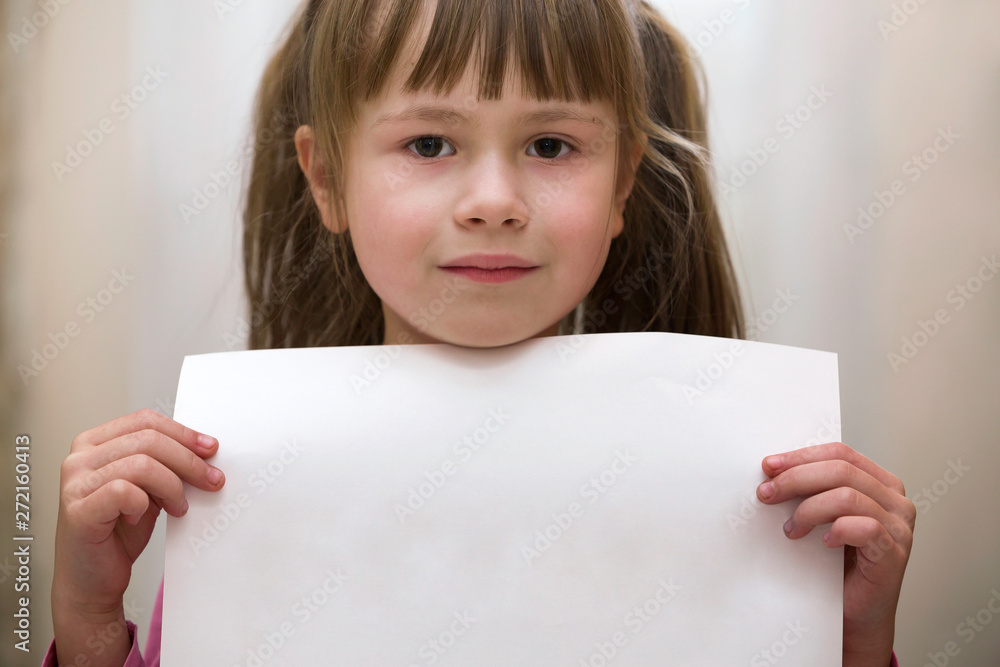 Happy smiling cute child girl holding white copy space sheet of drawing paper. Art education, creativity, advertisement concept. Happy smiling cute child girl holding white copy space sheet of drawing paper. Art education, creativity, advertisement concept.