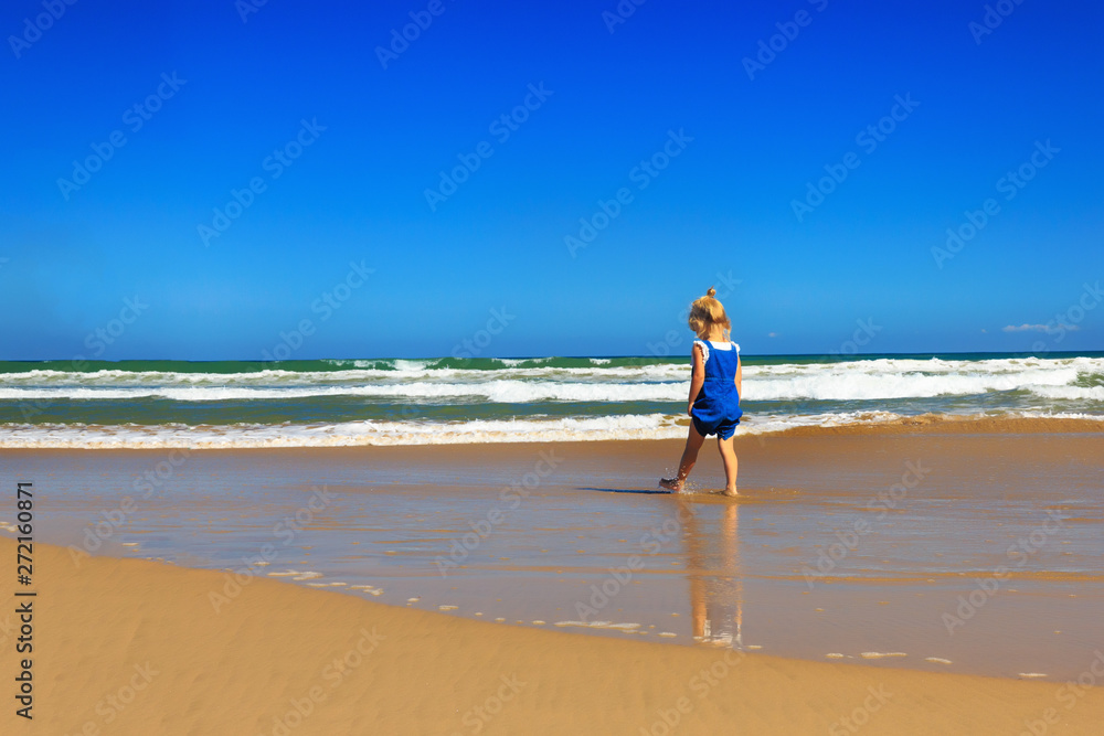 The girl is walking along the beach on a sunny day.