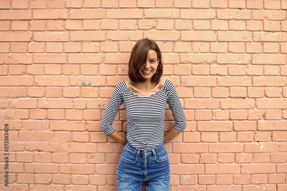 The girl is happy and smiling against the brick wall. Copy space, close up.